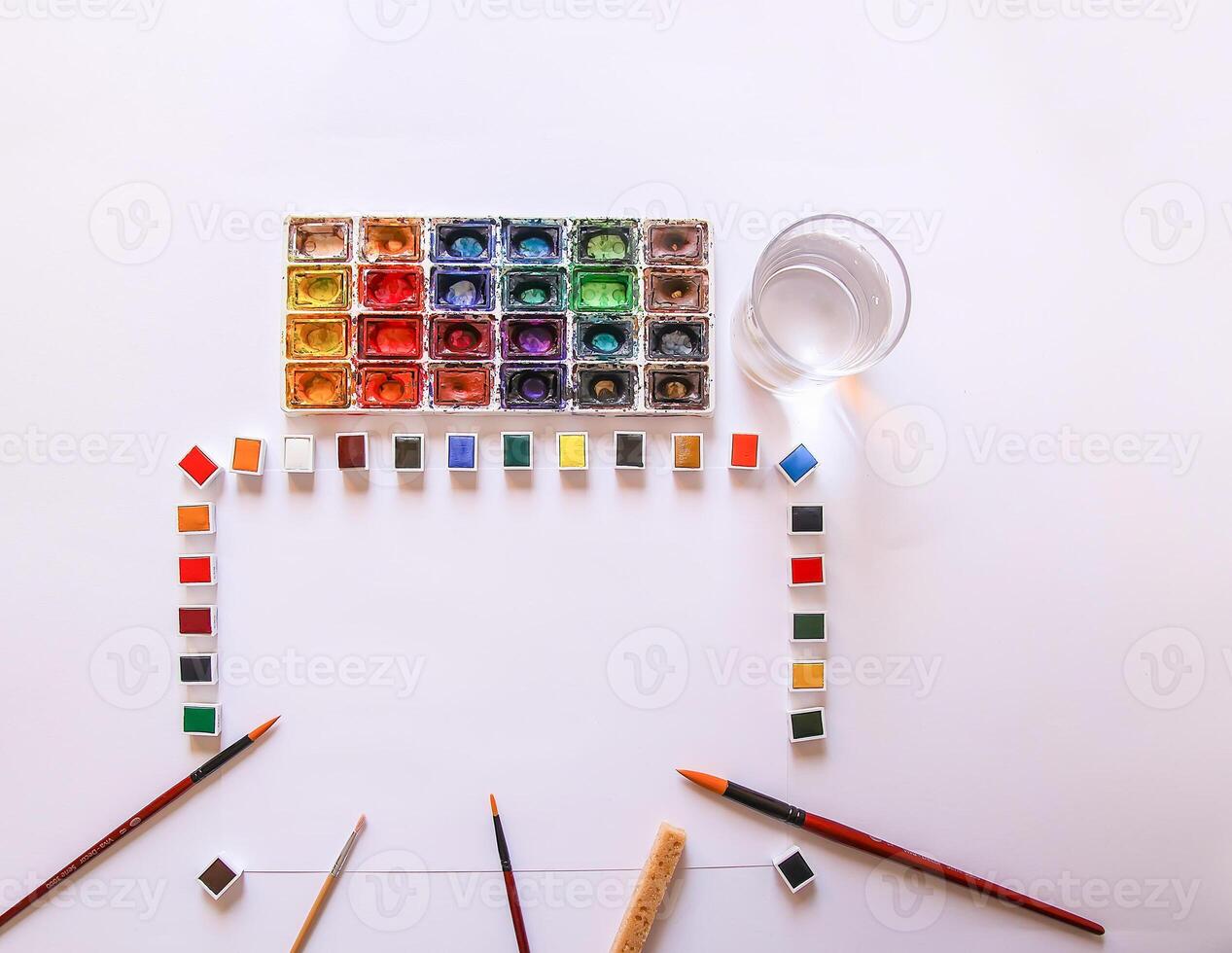 Watercolor paints, brushes, water in glass and paper on white background. Flat lay, top view photo