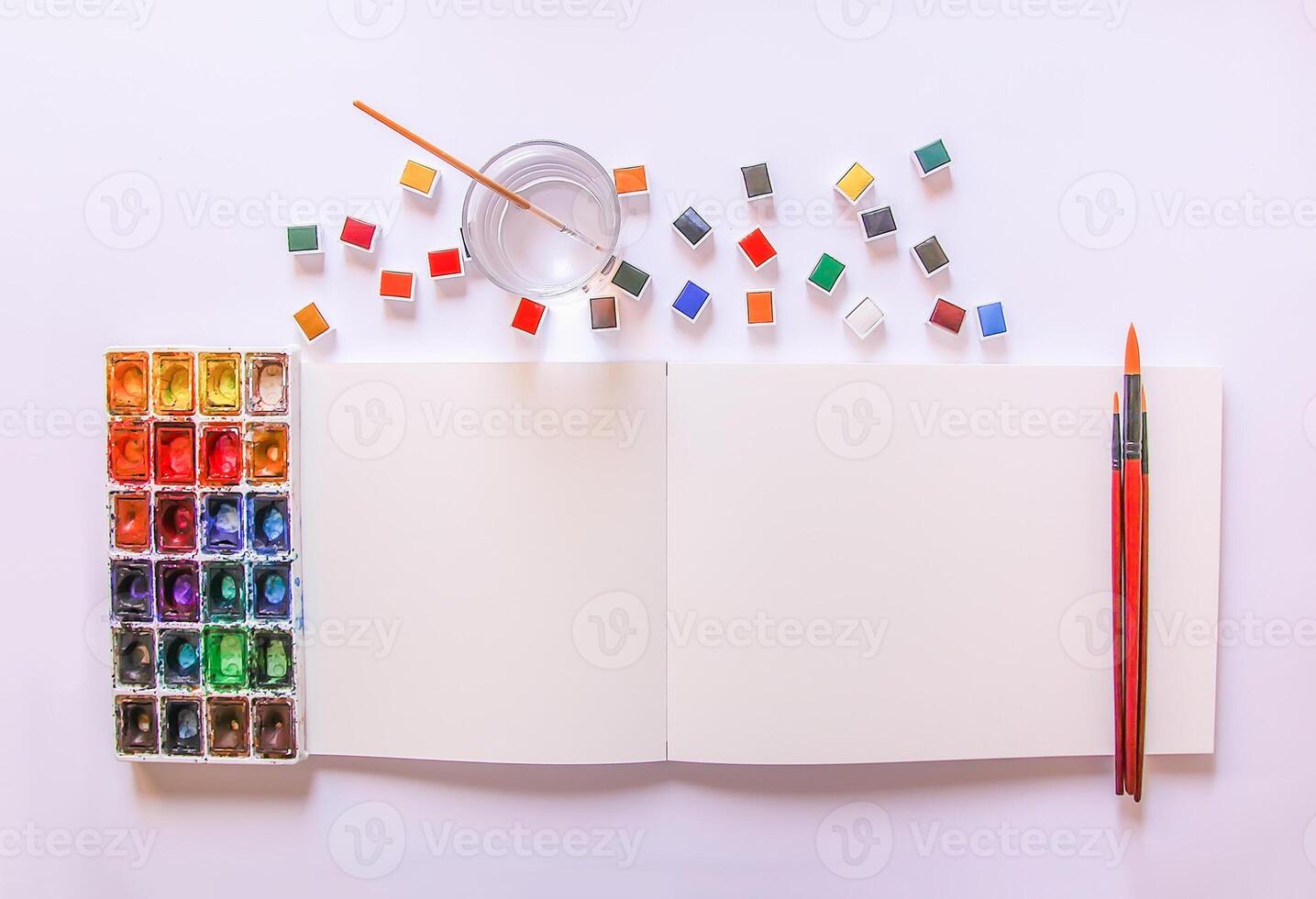 Watercolor paints, brushes, water in glass and paper on white background. Flat lay, top view photo