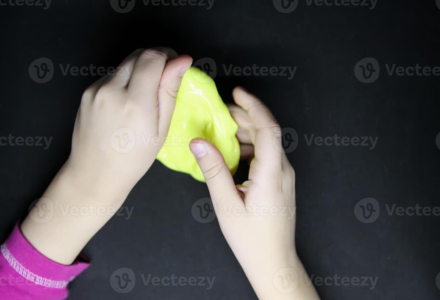 Girl playing with yellow slime in her hands. photo