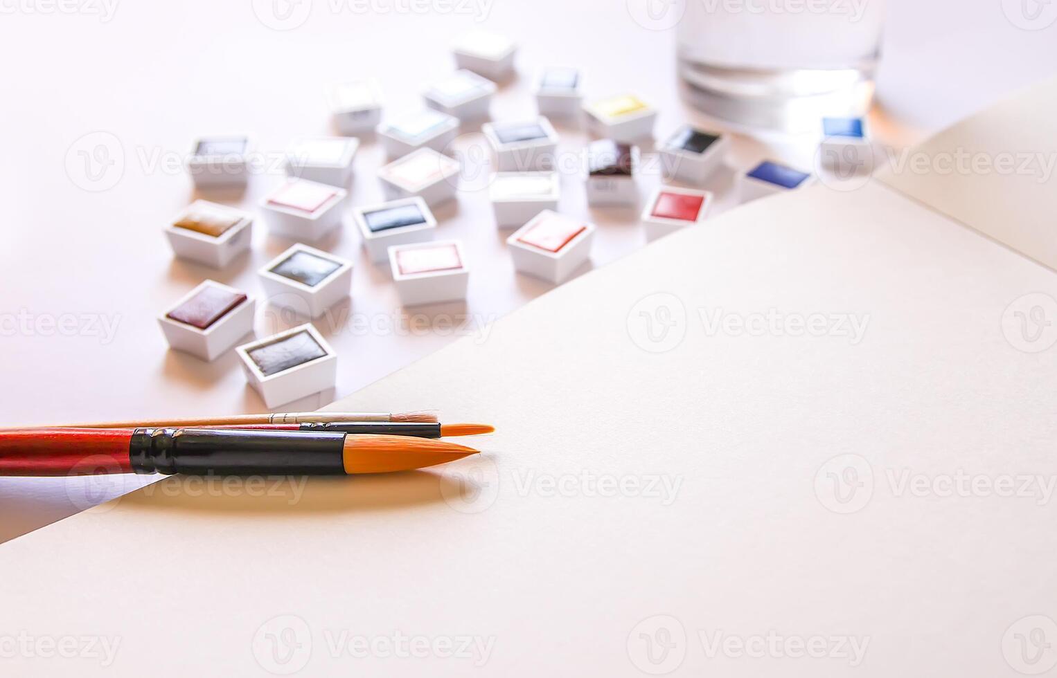Watercolor paints, brushes, water in glass and paper on white background. Flat lay, top view photo