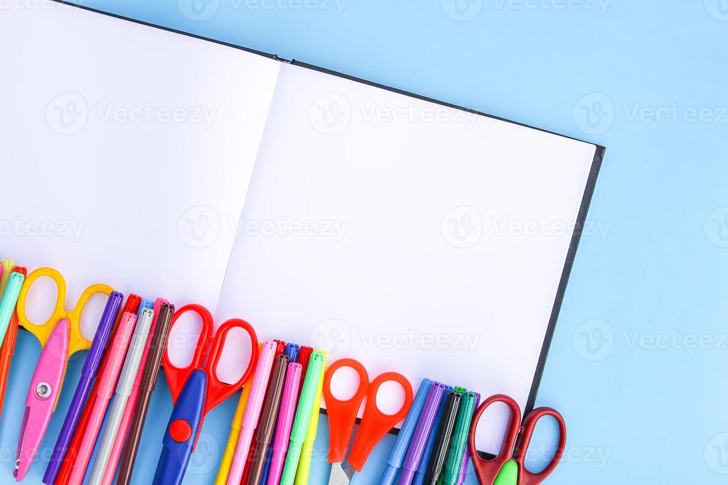 School supplies. Back to School design elements. Colorful markers and scissors on opened empty notepad on light blue paper background. photo