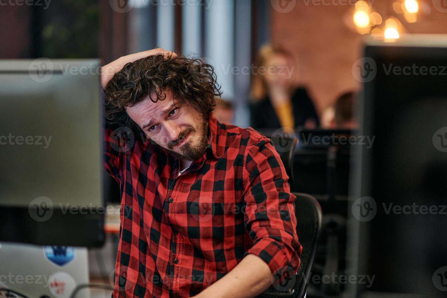 Disappointed Programmer with Messy Hair Looking at Computer Monitor in Office. photo
