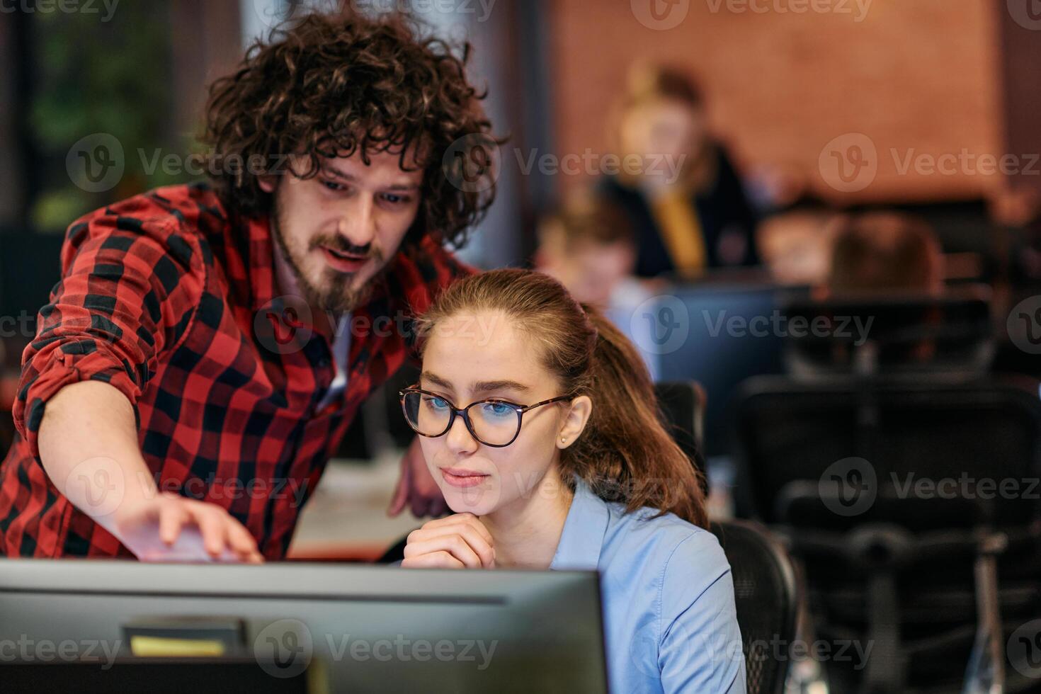 Business colleagues, a man and a woman, engage in discussing business strategies while attentively gazing at a computer monitor, epitomizing collaboration and innovation photo