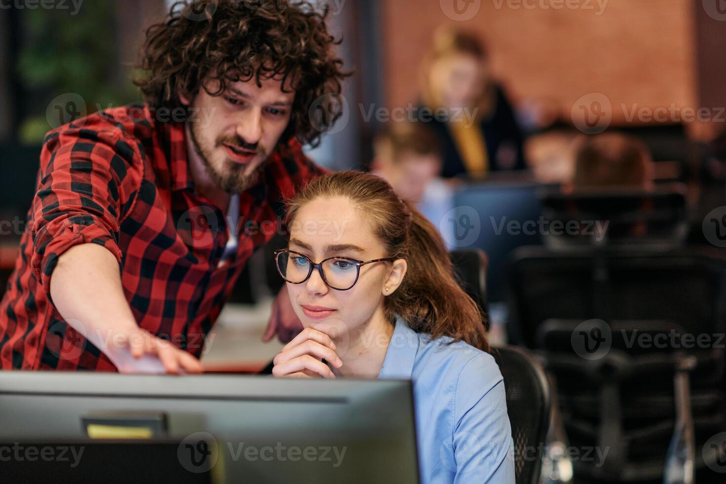Business colleagues, a man and a woman, engage in discussing business strategies while attentively gazing at a computer monitor, epitomizing collaboration and innovation photo