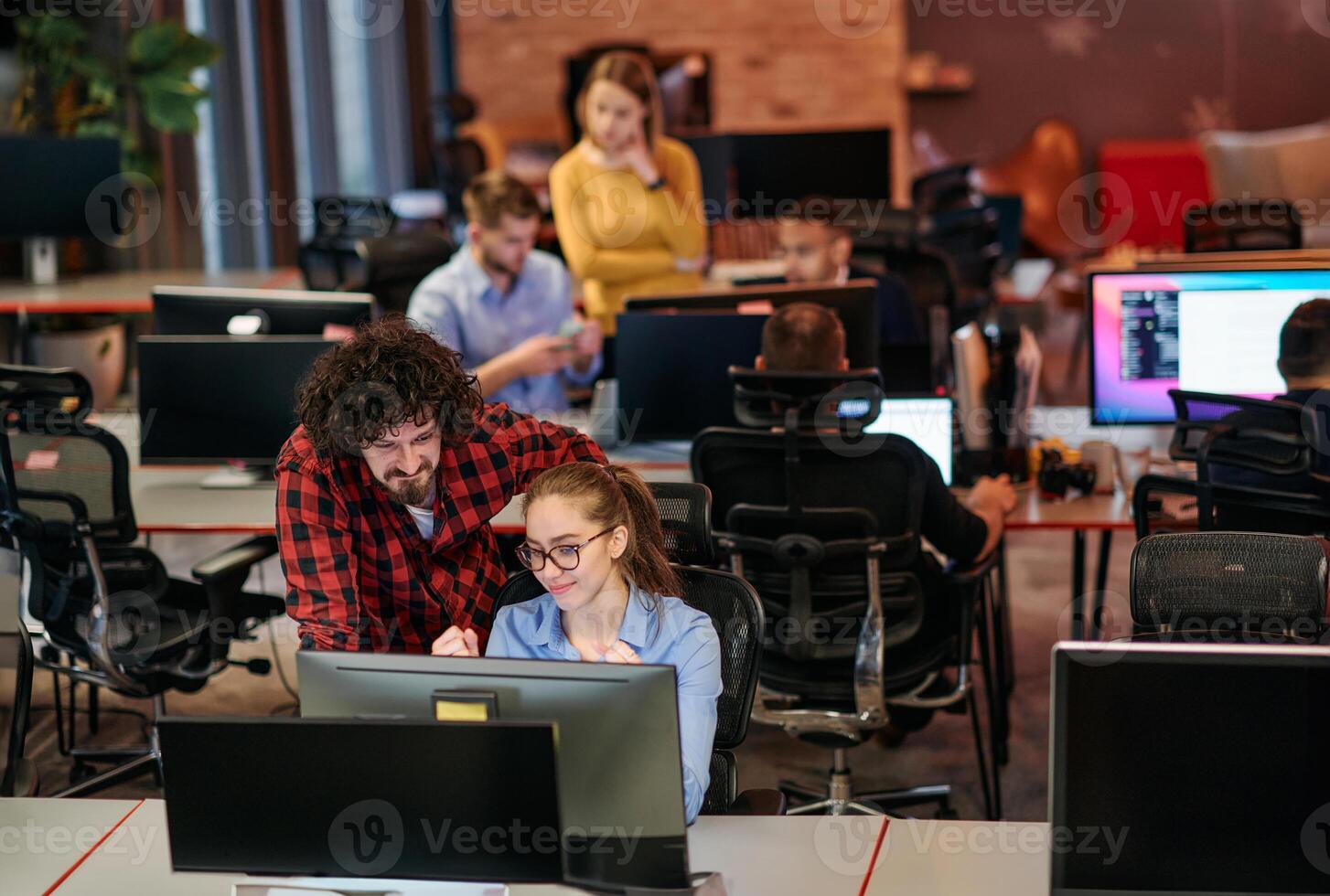 Business colleagues, a man and a woman, engage in discussing business strategies while attentively gazing at a computer monitor, epitomizing collaboration and innovation photo