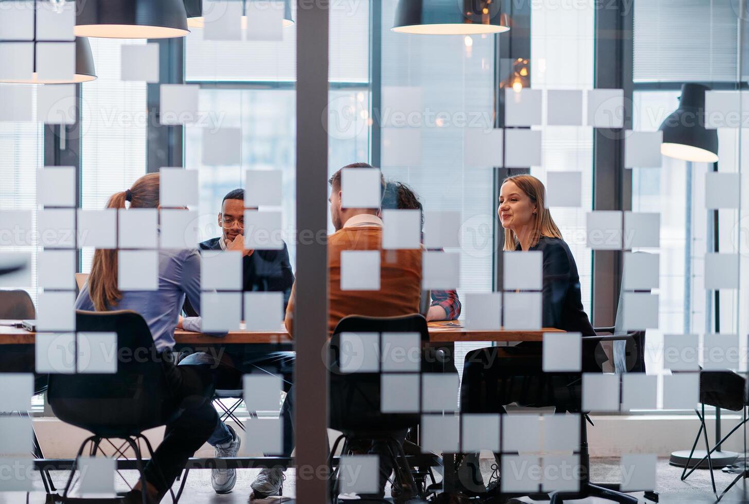 In a sleek glass office space, a team of business professionals engage in lively discussions and exchange strategic ideas, showcasing collaboration and innovation at the heart of modern corporate photo