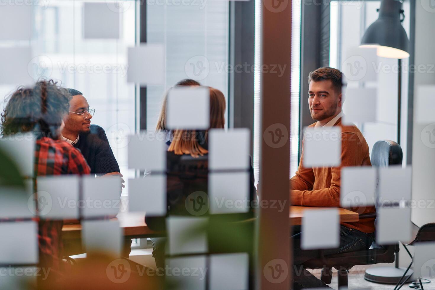 In a sleek glass office space, a team of business professionals engage in lively discussions and exchange strategic ideas, showcasing collaboration and innovation at the heart of modern corporate photo