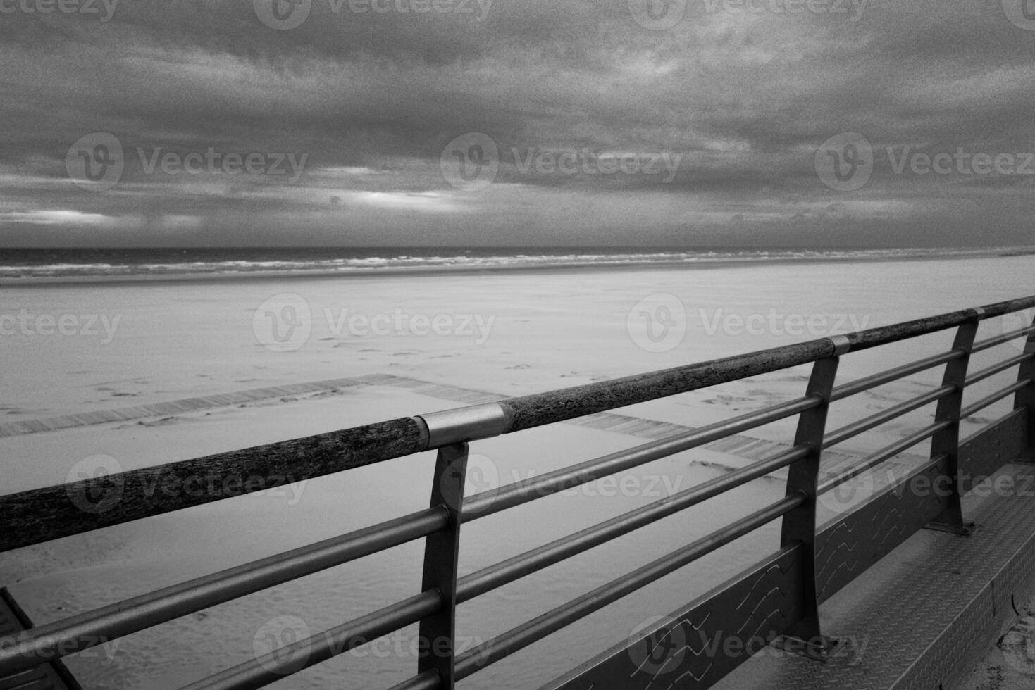 Metal railing in front of the empty beach and sea in the evening, greyscale shot photo