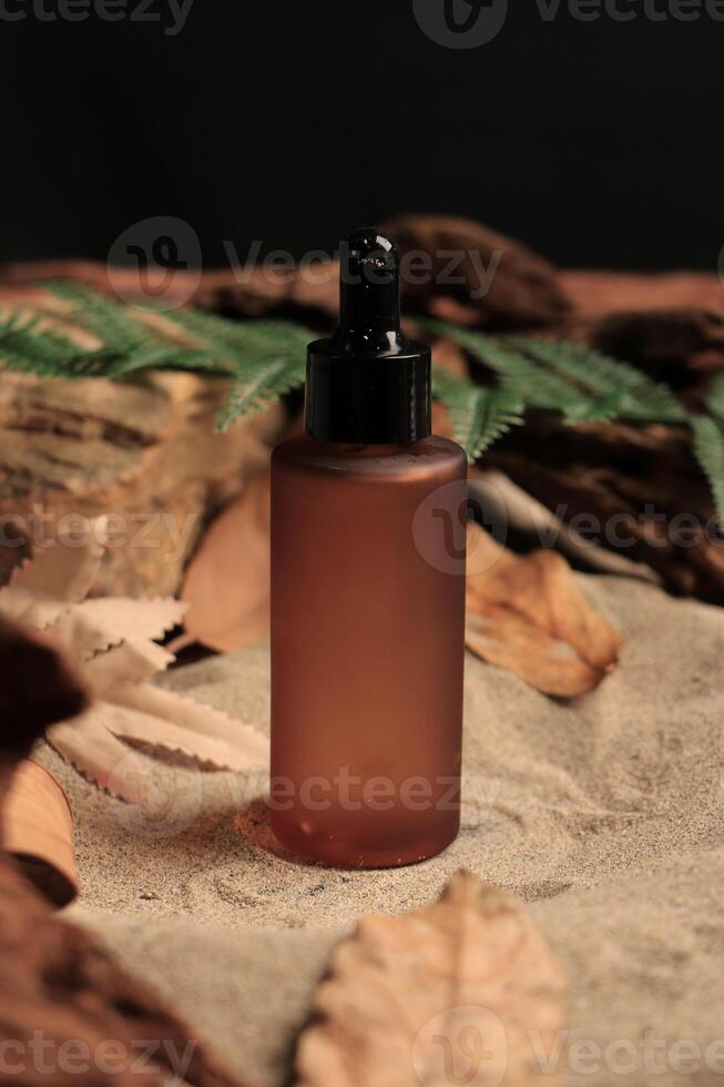 Amber Dropper Bottle on Natural Sand Background with Autumn Leaves and Ferns photo