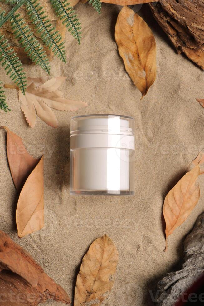 White Cosmetic Jar on Sandy Natural Background with Leaves photo