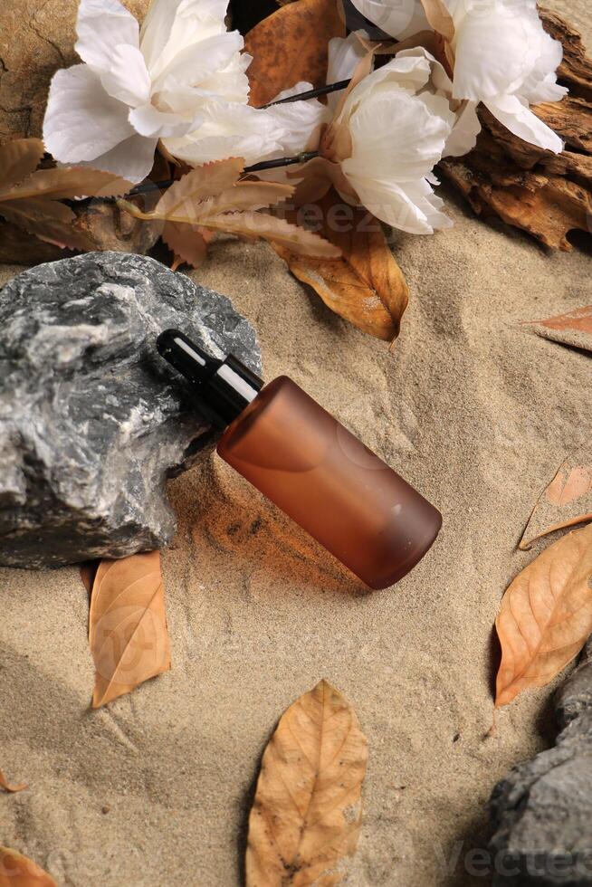 Amber Dropper Bottle with White Flowers and Autumn Leaves on Sandy Background photo