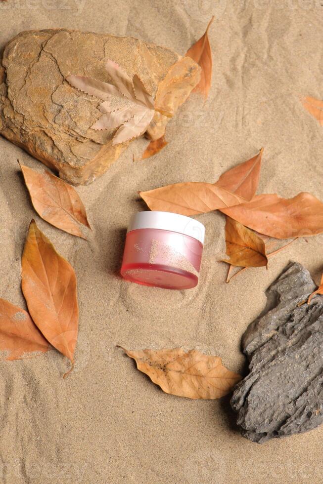 Pink Cosmetic Jar on Sandy Background with Autumn Leaves photo