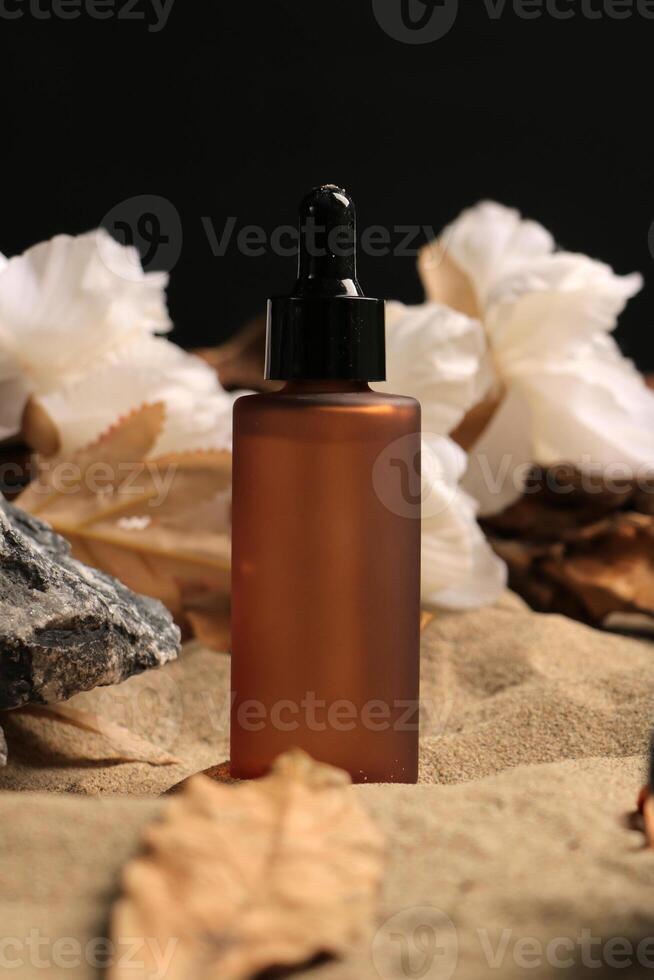 Amber Dropper Bottle with White Flowers on Sandy Background photo