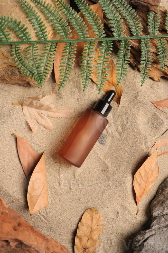 Amber Dropper Bottle on Sandy Background with Autumn Leaves and Ferns photo