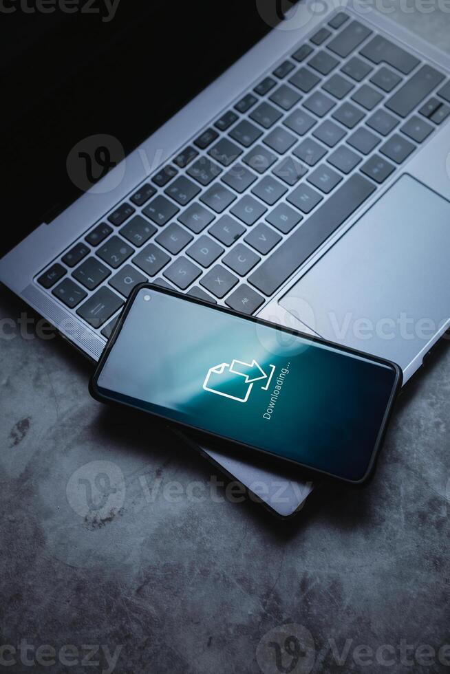 Smartphone laying on laptop whith download interface on screen. Cloud storage technology. Software update. Backup system. photo