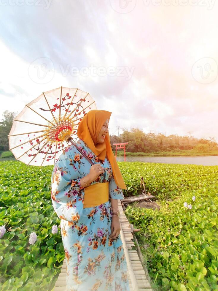 Charming Japanese woman wearing a kimono and holding an umbrella amidst stunning nature, captured at sunset photo