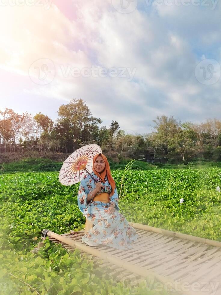Charming Japanese woman wearing a kimono and holding an umbrella amidst stunning nature, captured at sunset photo