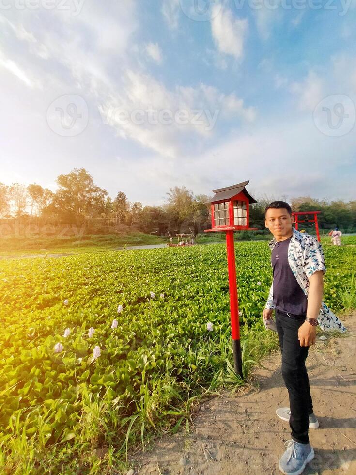 Cool asian man dressed in shirt is among the nature of amazing green leaves, enjoying a holiday looking for tranquility photo