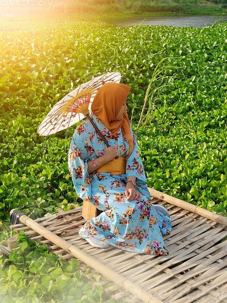 Charming Japanese woman wearing a kimono and holding an umbrella amidst stunning nature, captured at sunset photo