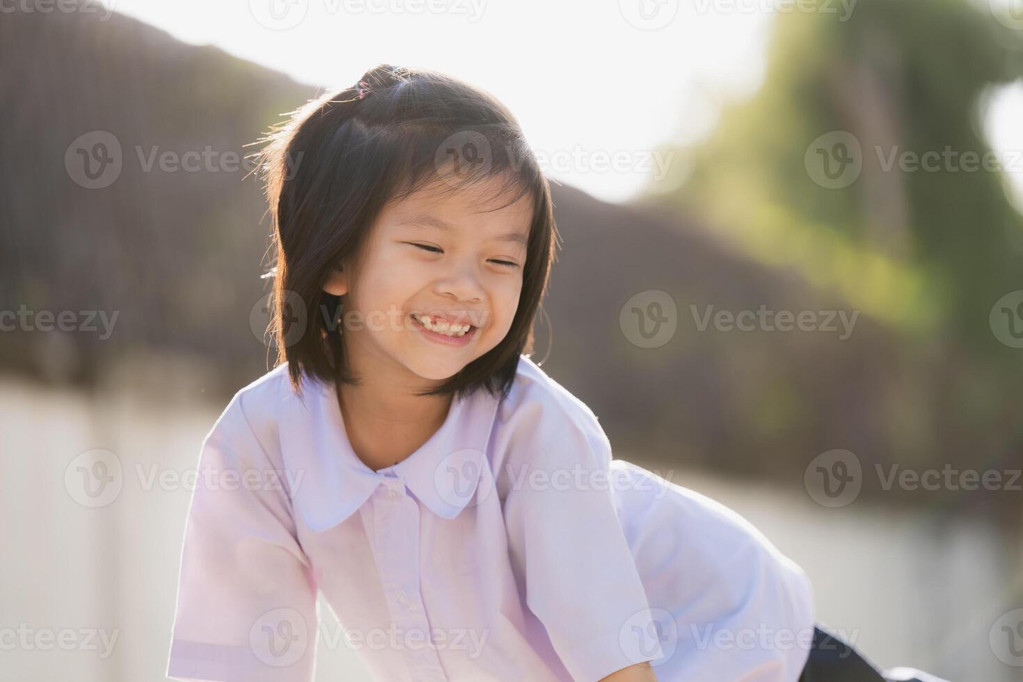 Portrait of smiling child in green park. A good-humored little girl with a sweet, bright smile. In the evenings after school, summer or spring, children are happy and cheerful. Kid wear school uniform photo