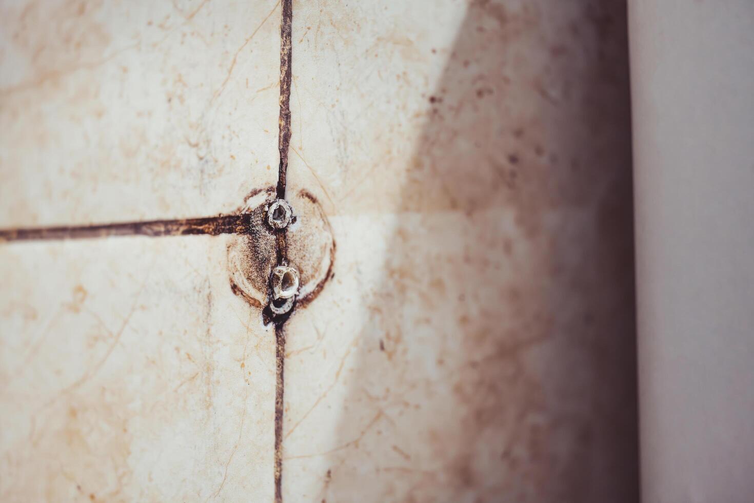 Closeup of Traces of holes in the tile grout with screws, old tiles with many scratches, black grout from dirt and mold. photo