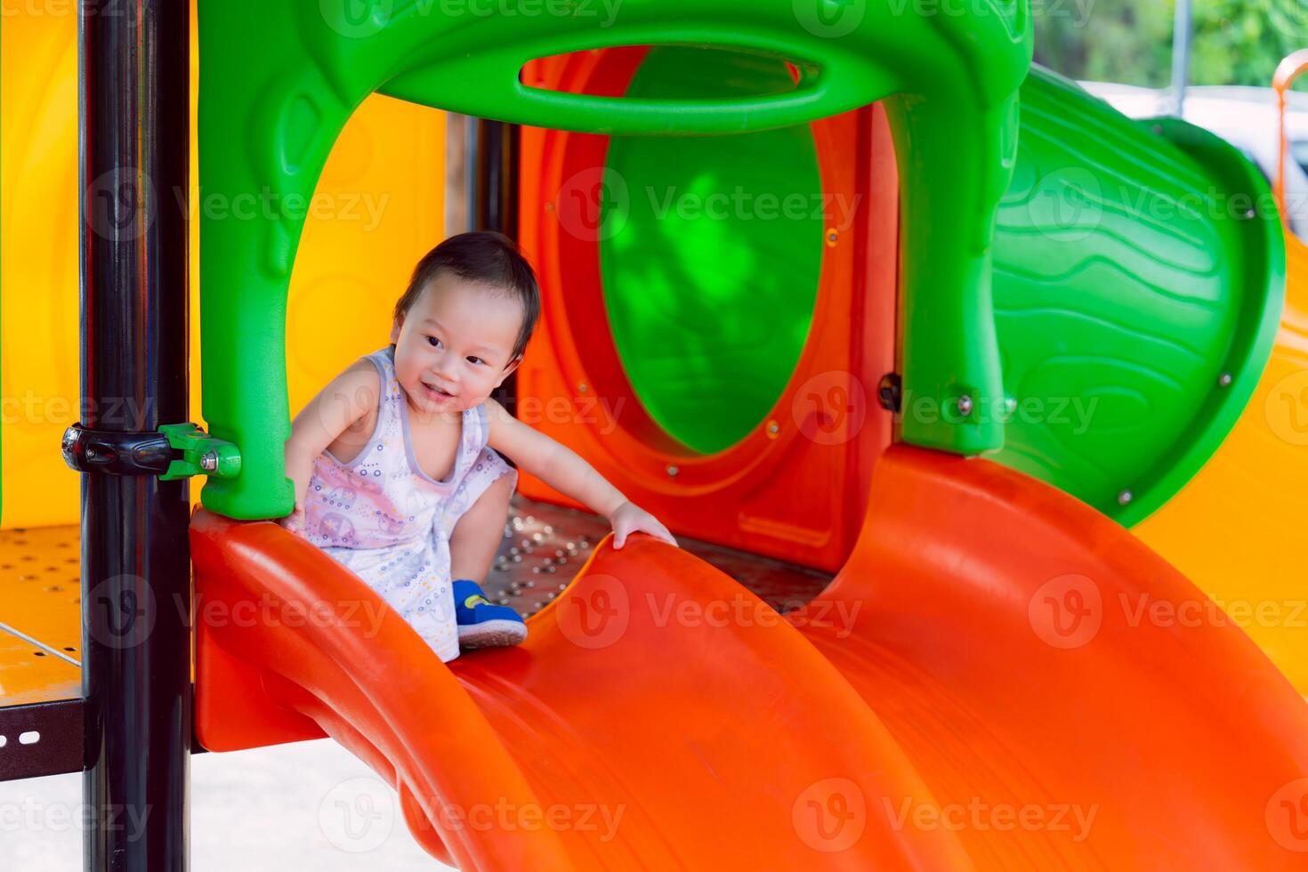 A boy having fun on a playground orange slide during summer. Muscle development. Asian toddler aged one year six month. photo