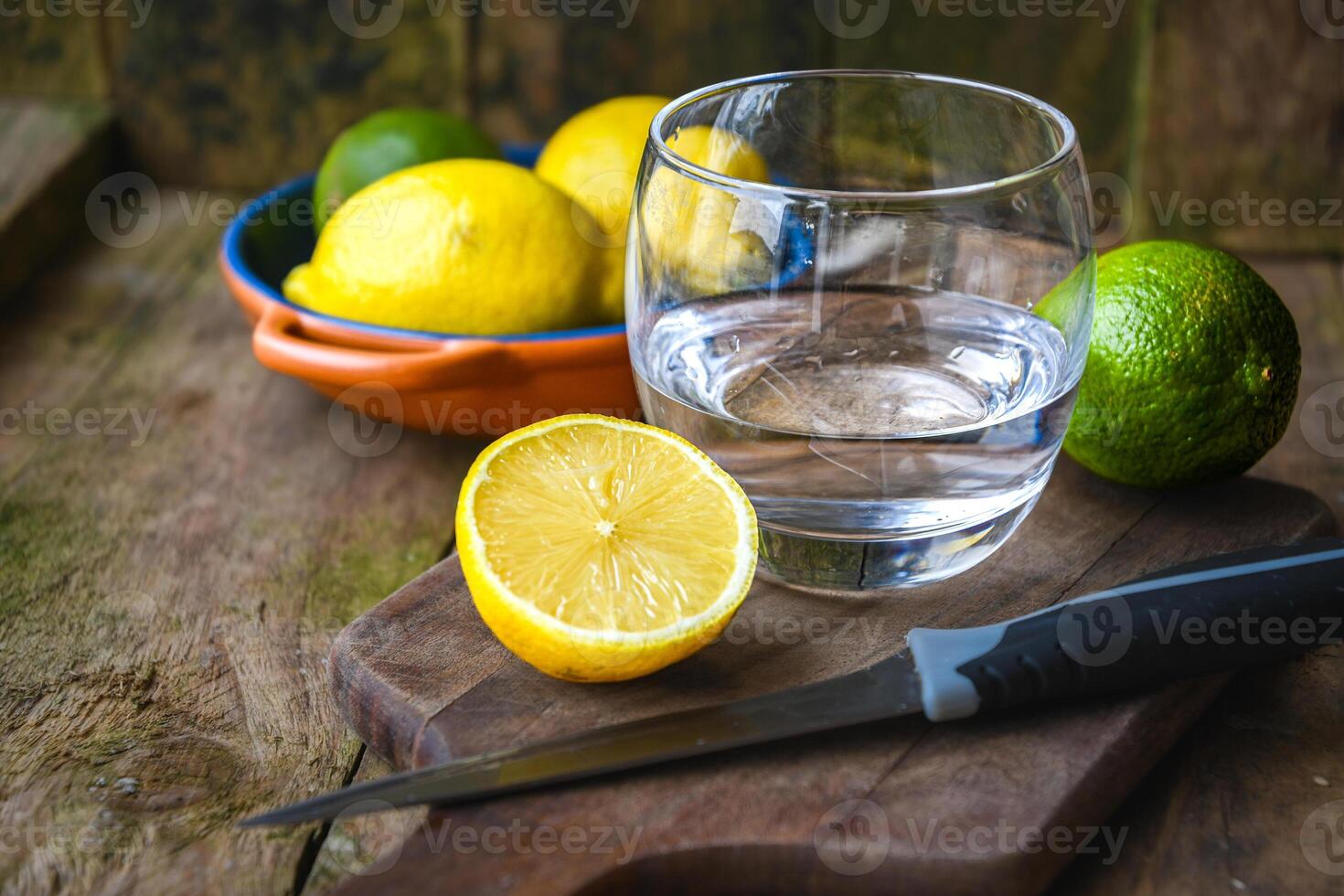 A glass of water and a ceramic plate with fruit, lemon, lime on a wooden table in a rustic kitchen. photo