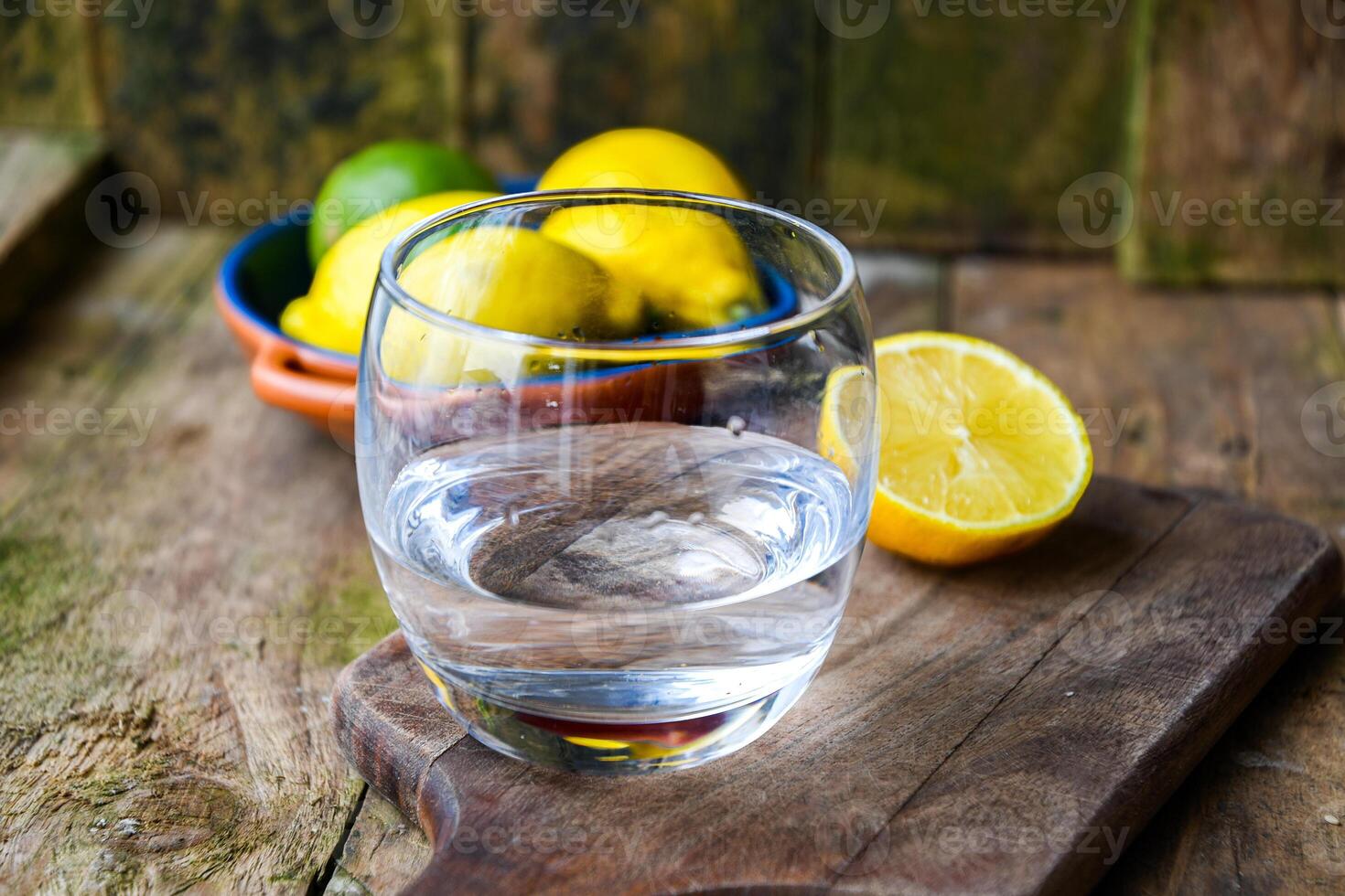 A glass of water and a ceramic plate with fruit, lemon, lime on a wooden table in a rustic kitchen. photo
