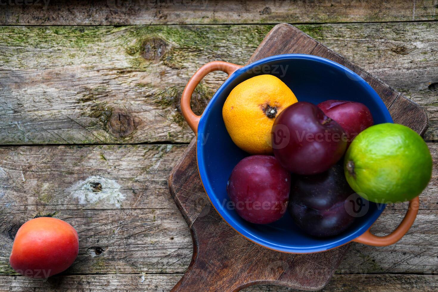 plums, lime, tangerine in a ceramic bowl and apricot on a wooden table photo