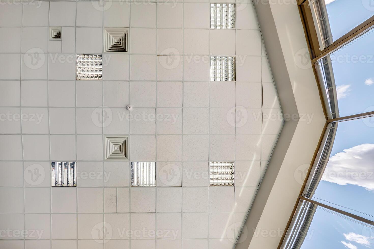 cassette stretched or suspended ceiling with square halogen spots lamps and drywall construction in empty room in house or office. Looking up view photo