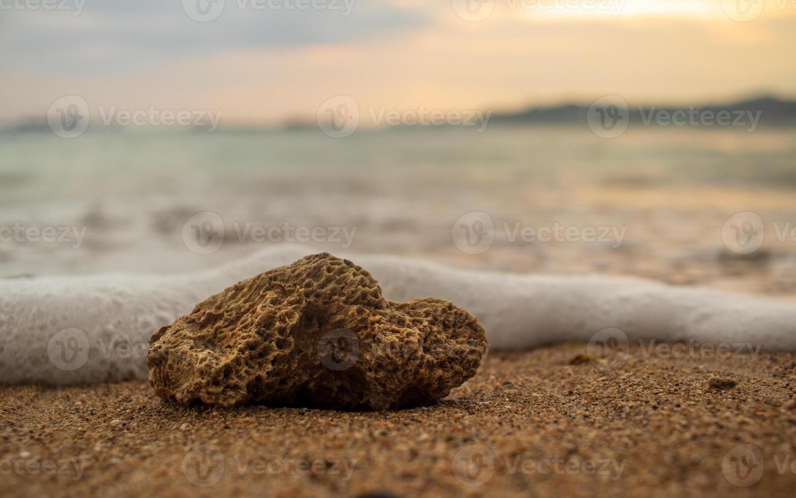 Closeup shot of a stone in the sand of beach with foam photo
