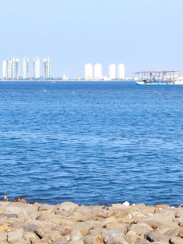 a view of the sea on a clear day, there are tall buildings and fishing boats passing by on the sea. photo