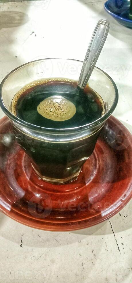 A glass of hot black coffee on a small plate photo