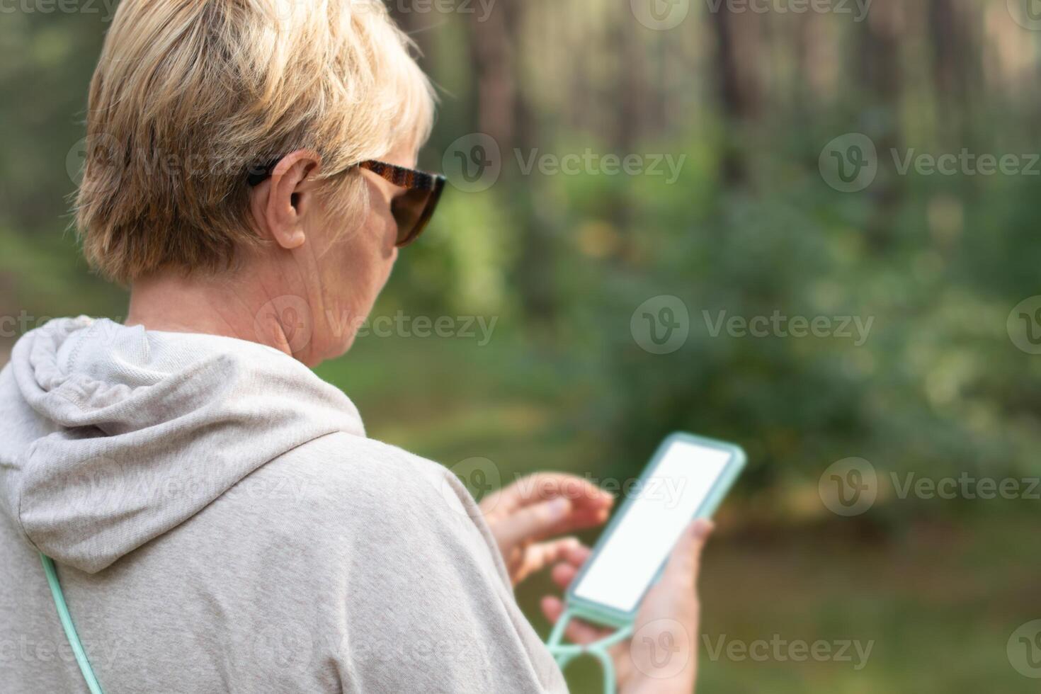 middle-aged woman in the forest takes daily steps, looks at the route map on her smartphone, turns on the pedometer, white screen mockup soft focus photo