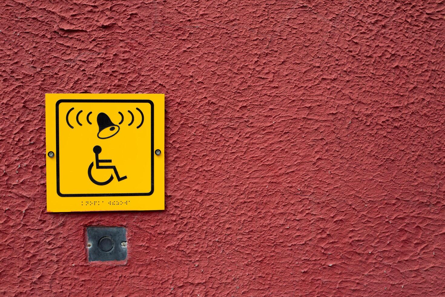 Wheelchair icon with bell and braille text on red wall next to button to call help for disabled person photo
