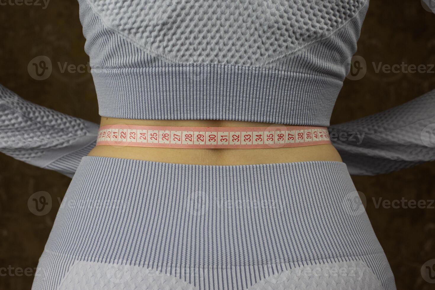 Rear view of back of thin girl with flexible tape wrapped around her body for measuring waist circumference, sport and healthy lifestyle concept photo