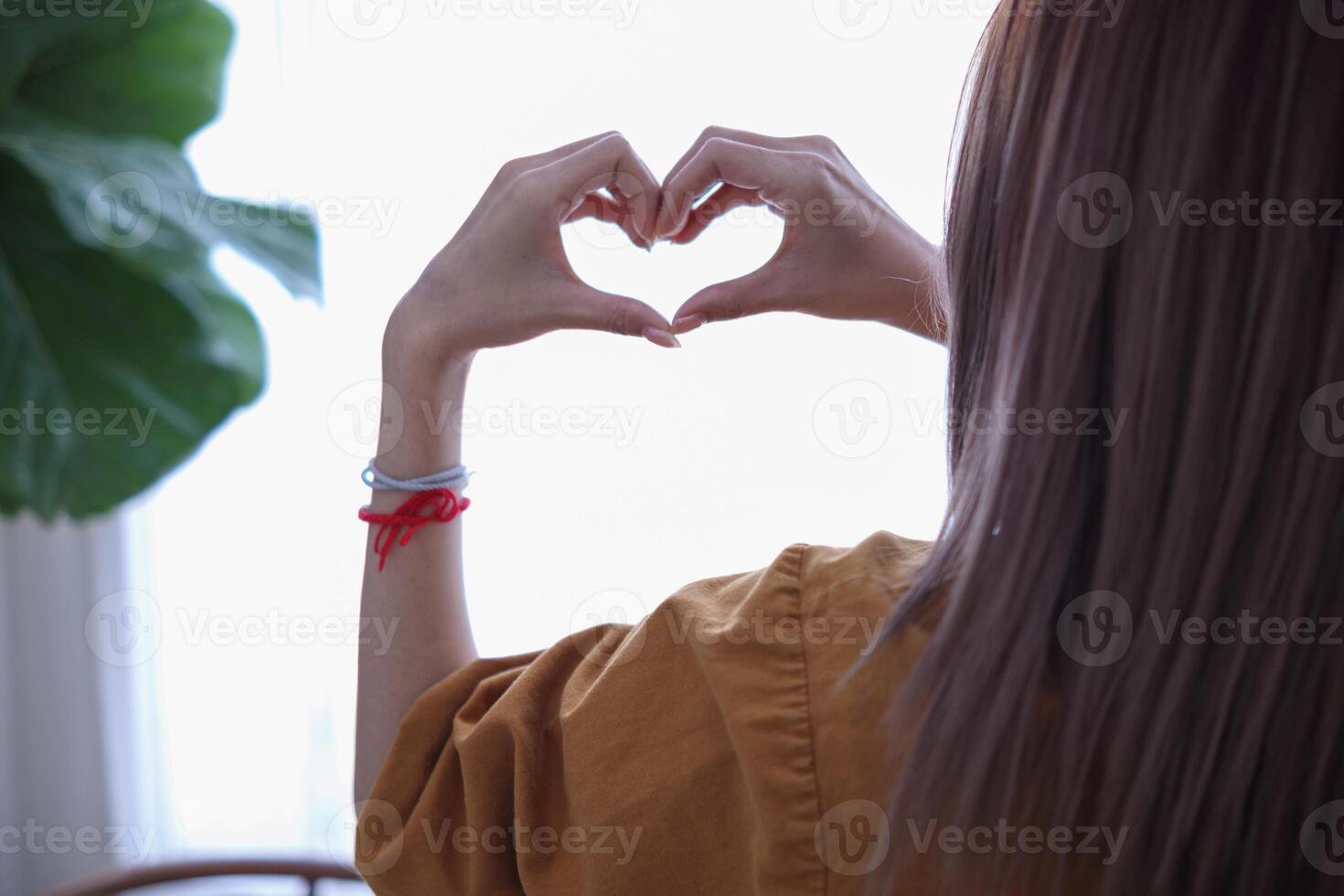 A young woman raises her hands above to make a heart symbol that means friendship love and kindness on a beautiful morning blurred background Friendship and love concept photo