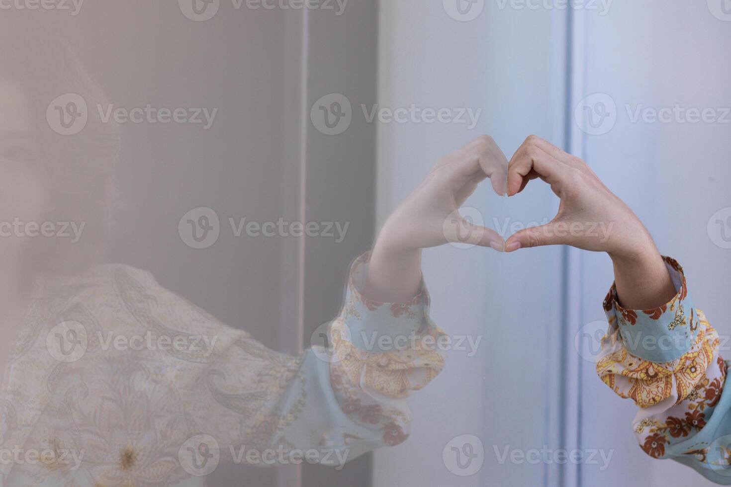 A young woman raises her hands above to make a heart symbol that means friendship love and kindness on a beautiful morning blurred background Friendship and love concept photo