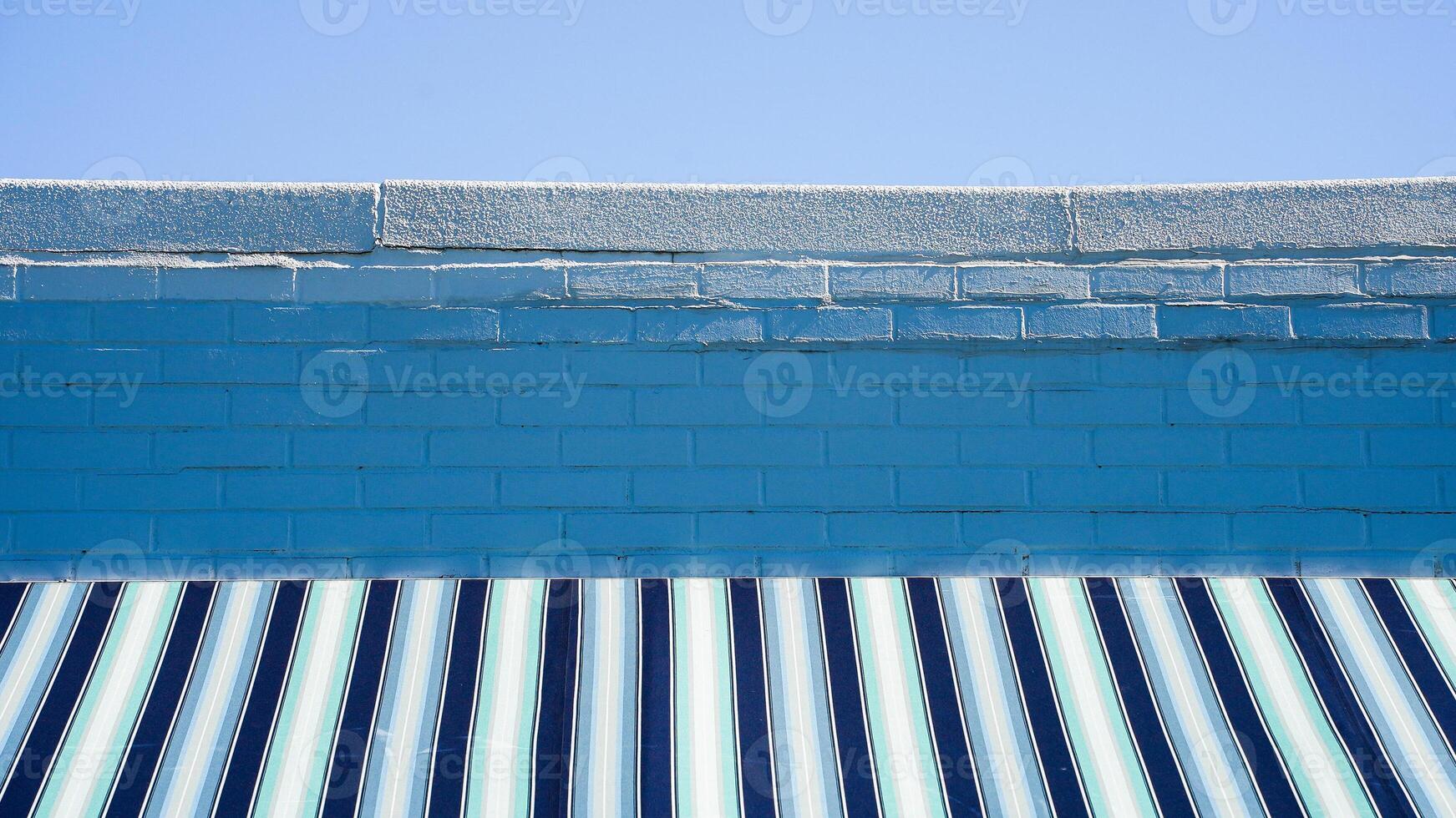 A close-up shot of a blue brick wall with a striped awning underneath photo