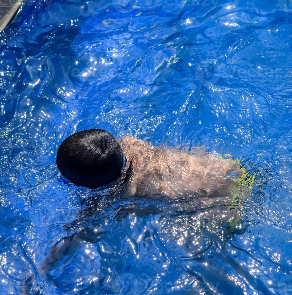 Happy Indian boy swimming in a pool, Kid wearing swimming costume along with air tube during hot summer vacations, Children boy in big swimming pool. photo
