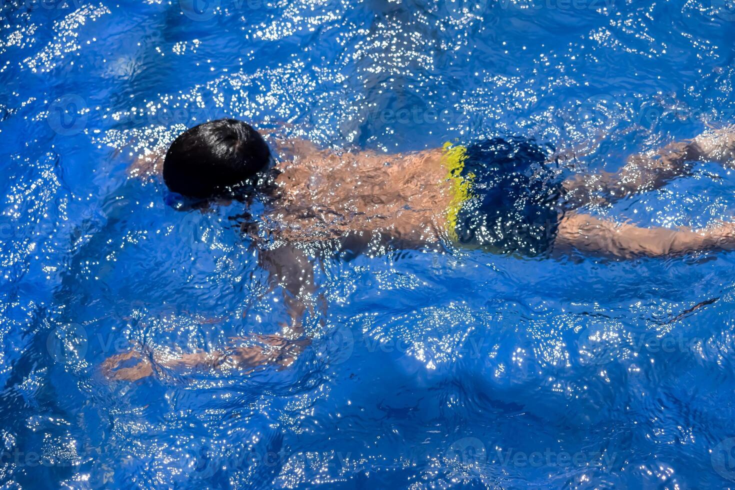 Happy Indian boy swimming in a pool, Kid wearing swimming costume along with air tube during hot summer vacations, Children boy in big swimming pool. photo