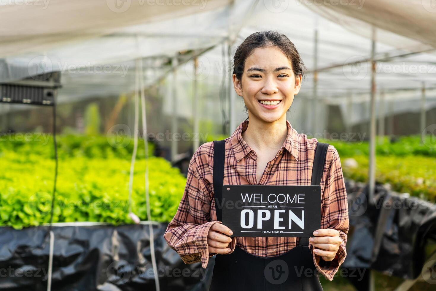 Portrait of young asian woman farmer holding open sign on hydroponics organic vegetable farm, Owner female of the hydroponics salad garden takes customer orders to pack fresh vegetables. photo