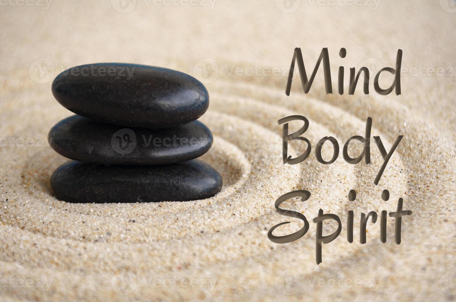 Mind, body and spirit text with black Zen stones on sand background photo