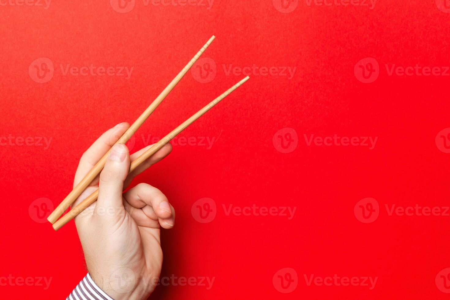 Male hand with chopsticks on red background. Traditional asian food with emty space for your design photo