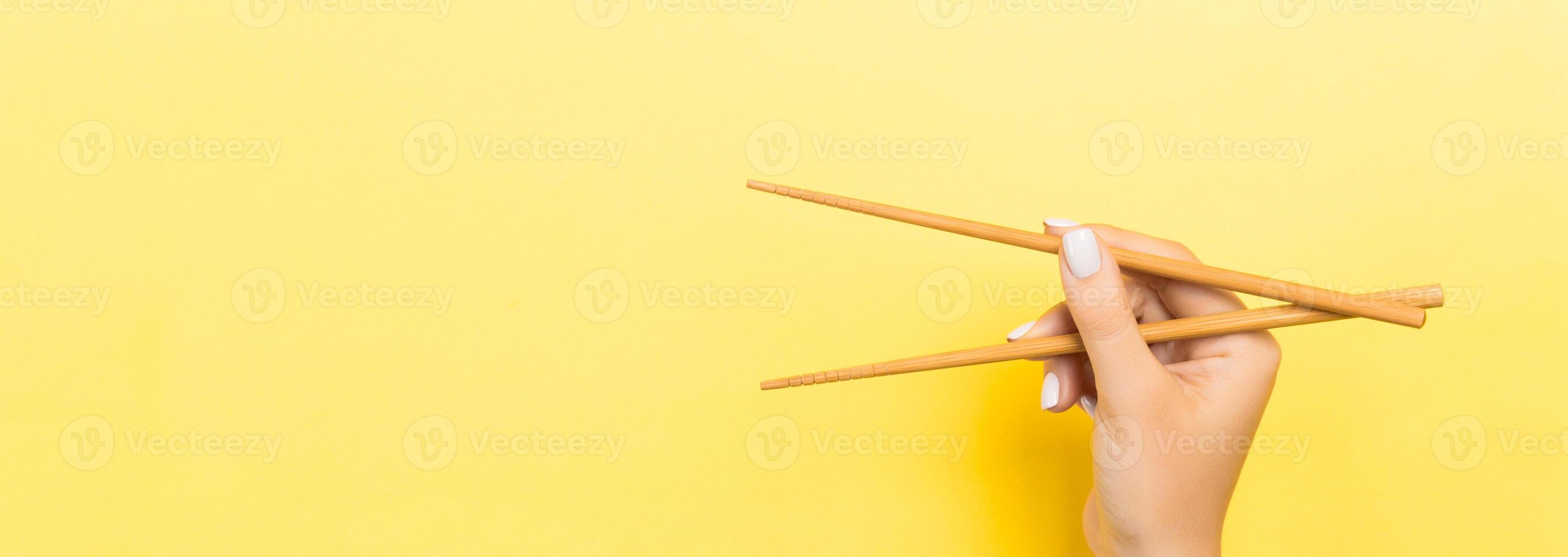 Wooden chopsticks holded with female hands on yellow background. Ready for eating concepts with empty space photo
