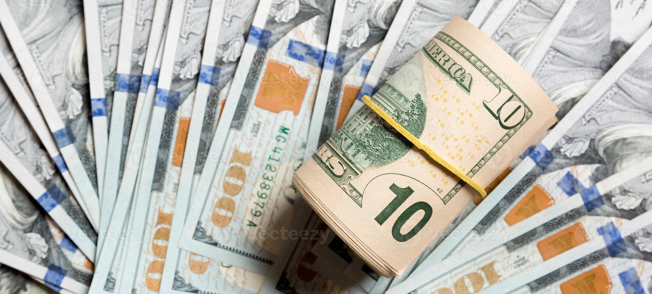 Top view of 10 rolled dollar bills on background made with one hundred dollar banknotes. Business concept photo