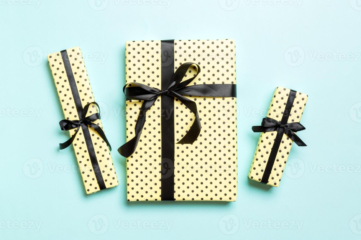 wrapped Christmas or other holiday handmade present in paper with Black ribbon on blue background. Present box, decoration of gift on colored table, top view photo