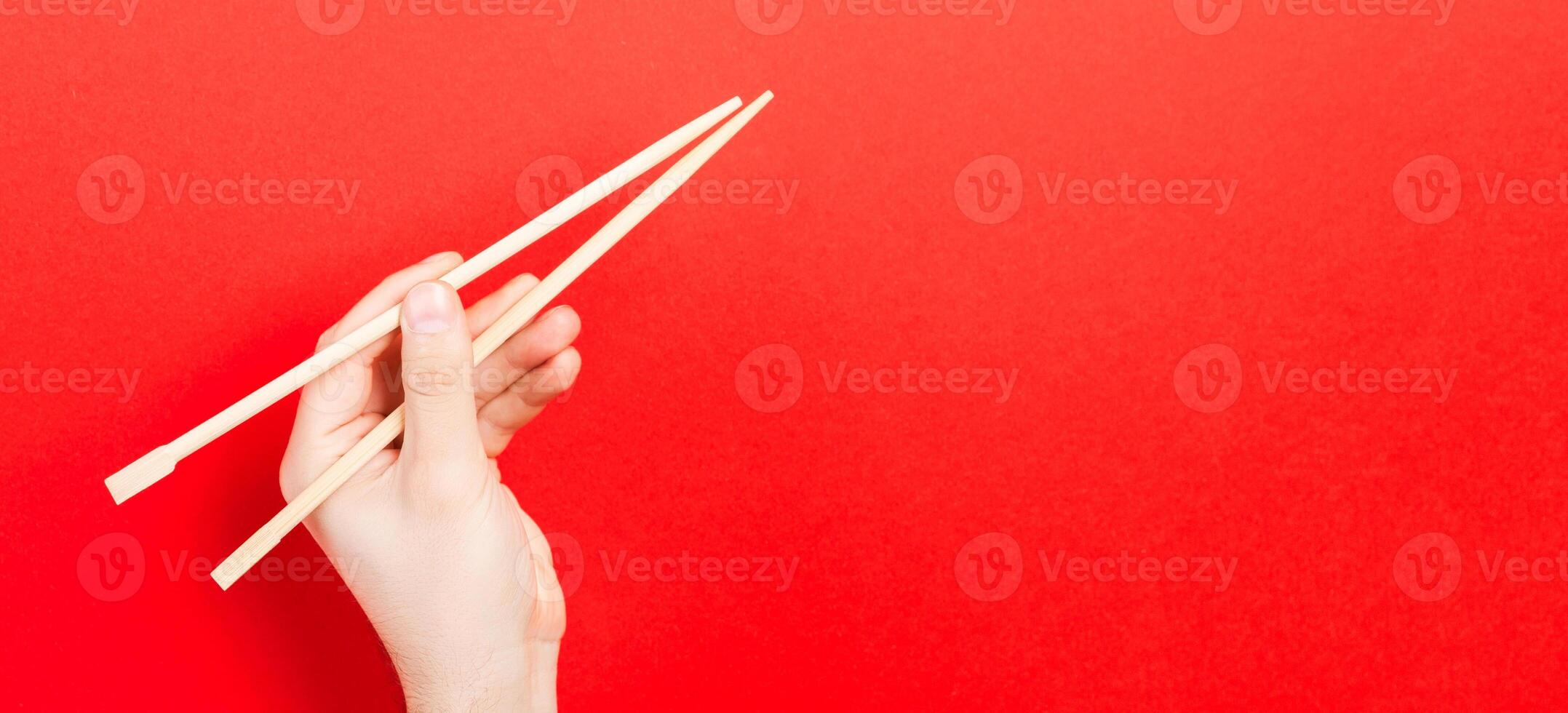 Wooden chopsticks in male hand on red background with empty space for your idea. Tasty food concept photo