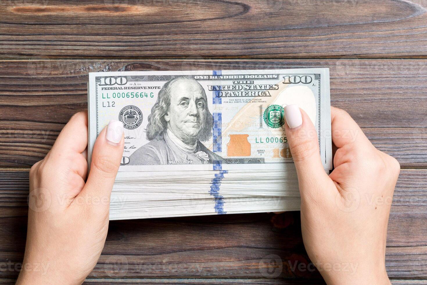 Top view of one hundred dollar banknotes in female hands on wooden background. Business and financial concept photo