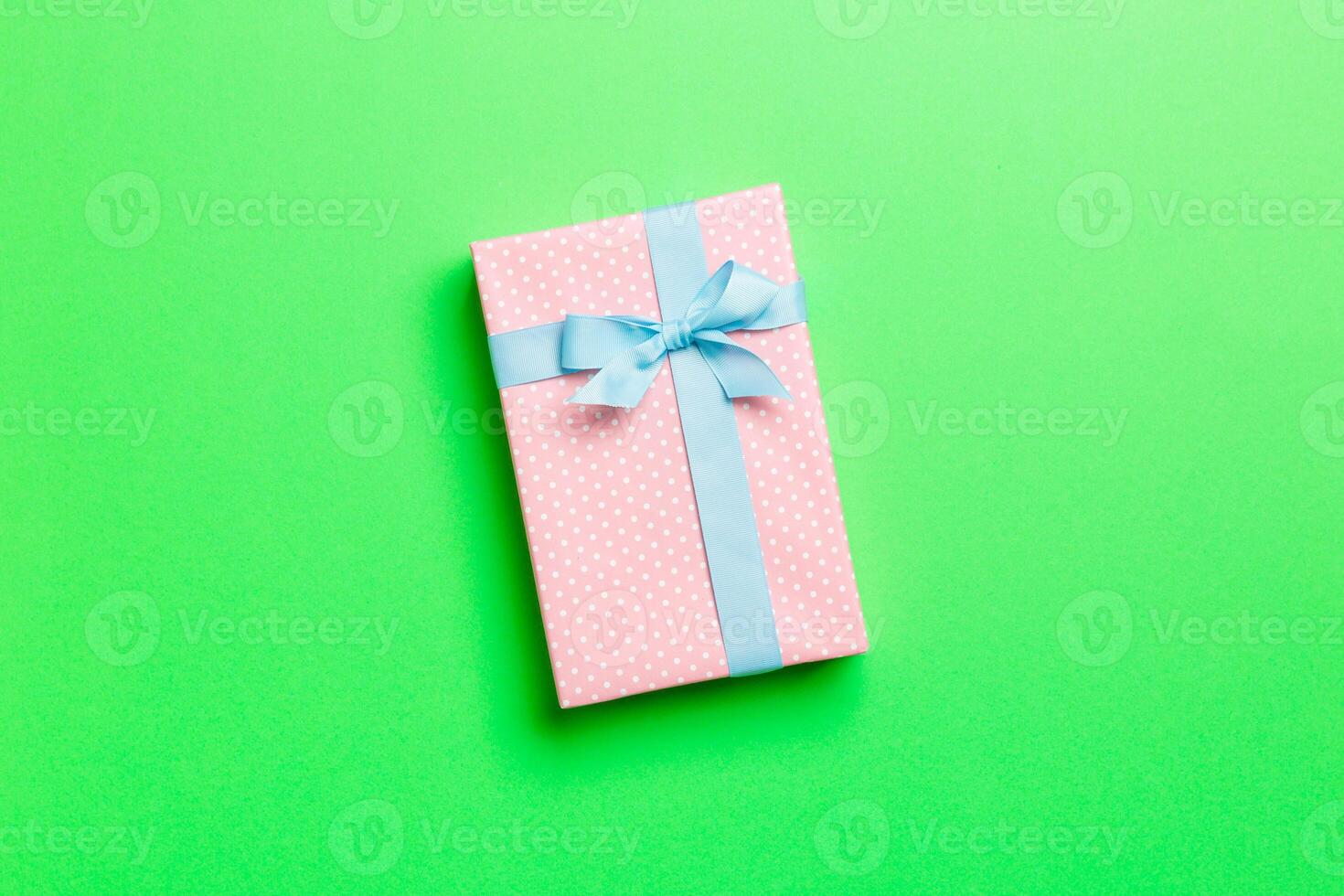 wrapped Christmas or other holiday handmade present in paper with blue ribbon on green background. Present box, decoration of gift on colored table, top view with copy space photo